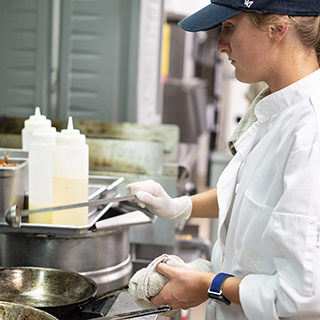 Graduate student in a commercial teaching kitchen preparing food during a nutrition and hospitality management master's program at the University of Mississippi.