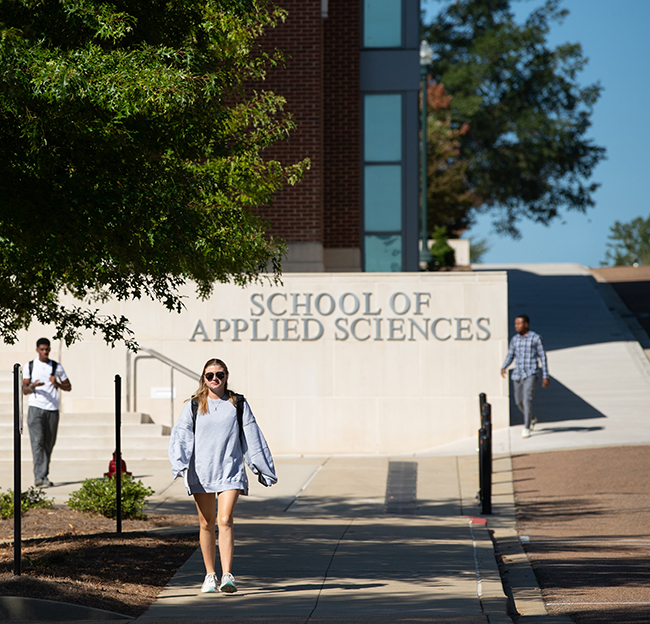 Students walk near the University of Mississippi School of Applied Sciences building on a sunny day.