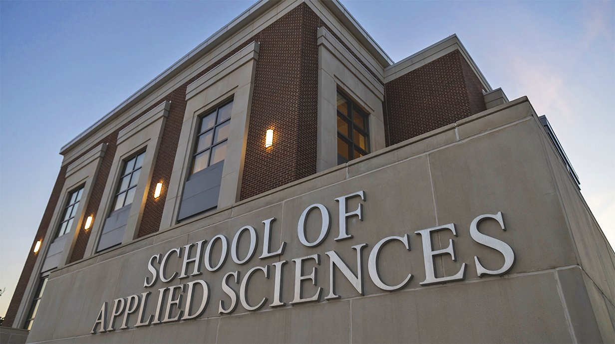 Exterior view of the University of Mississippi School of Applied Sciences building, featuring the school name displayed prominently on a stone facade at dusk.