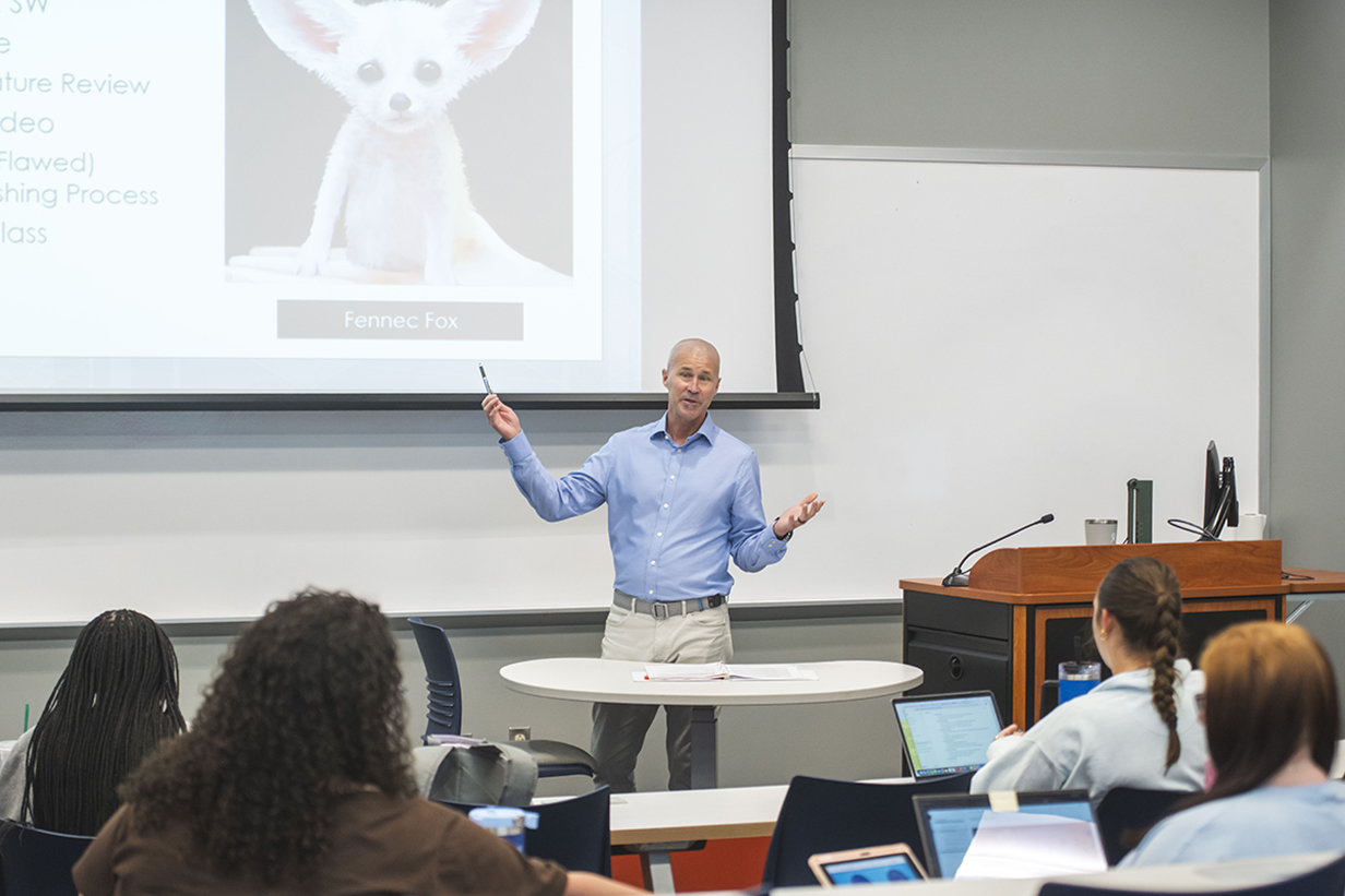 Professor lectures to social work students in a classroom equipped with laptops and presentation technology.