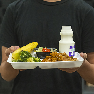 Student holds a nutritious school meal tray with vegetables, fruit, milk, and an entree as part of child nutrition research and education.