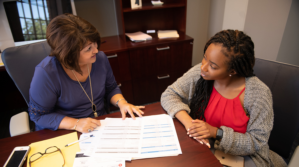A School of Applied Sciences student sits with an advisor at a table with papers and a laptop sitting in front of them.
