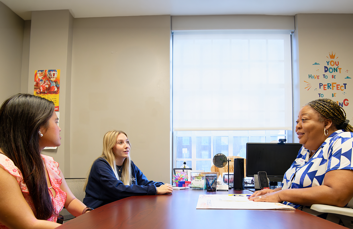 Academic advisor meets with two students in an office, discussing academic planning and student success resources.